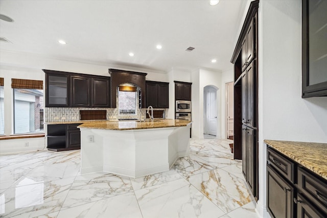 kitchen with sink, stainless steel microwave, light stone countertops, and a kitchen island with sink