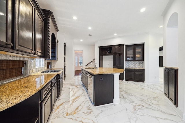 kitchen featuring dark brown cabinetry, sink, decorative backsplash, light stone counters, and a kitchen island with sink