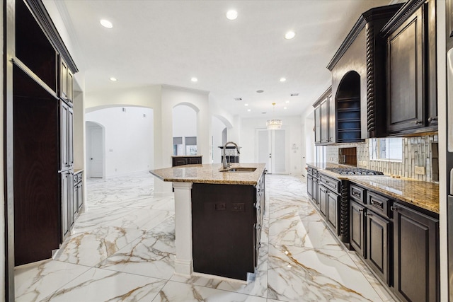 kitchen featuring a kitchen bar, light stone countertops, sink, pendant lighting, and an island with sink