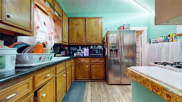 kitchen featuring stainless steel appliances, light hardwood / wood-style flooring, and dark stone counters