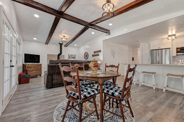 dining room featuring a chandelier, light hardwood / wood-style floors, and vaulted ceiling with beams