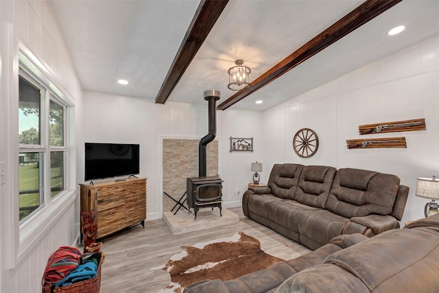 living room featuring light hardwood / wood-style floors, a wood stove, lofted ceiling with beams, and a notable chandelier