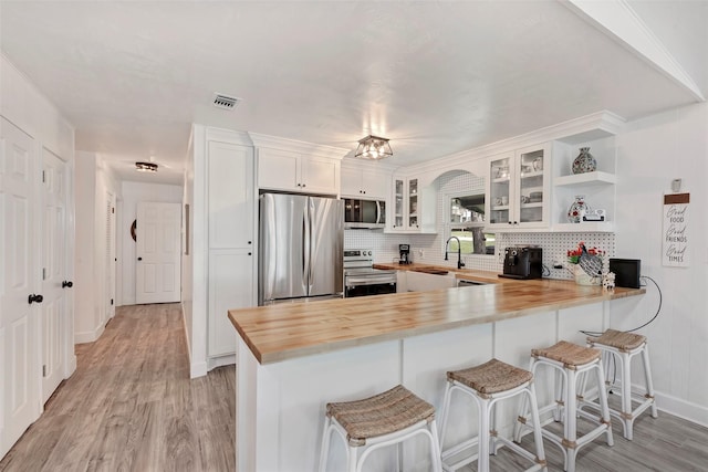 kitchen with white cabinetry, butcher block countertops, kitchen peninsula, and stainless steel appliances