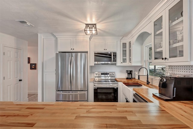 kitchen featuring butcher block counters, appliances with stainless steel finishes, backsplash, white cabinets, and sink