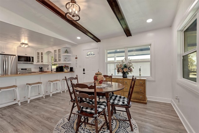 dining area with lofted ceiling with beams, sink, an inviting chandelier, and light hardwood / wood-style floors