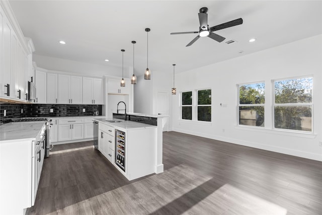 kitchen featuring a kitchen island with sink, hanging light fixtures, light stone counters, sink, and white cabinetry