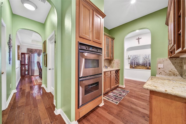 kitchen featuring double oven, backsplash, light stone countertops, and dark wood-type flooring