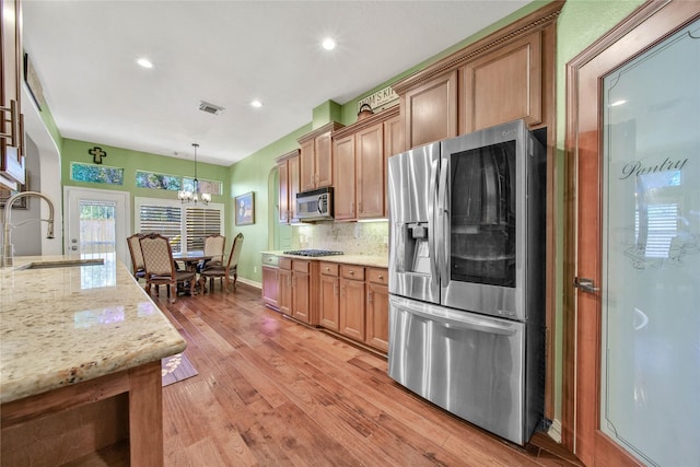 kitchen with sink, light stone countertops, light wood-type flooring, decorative light fixtures, and stainless steel appliances