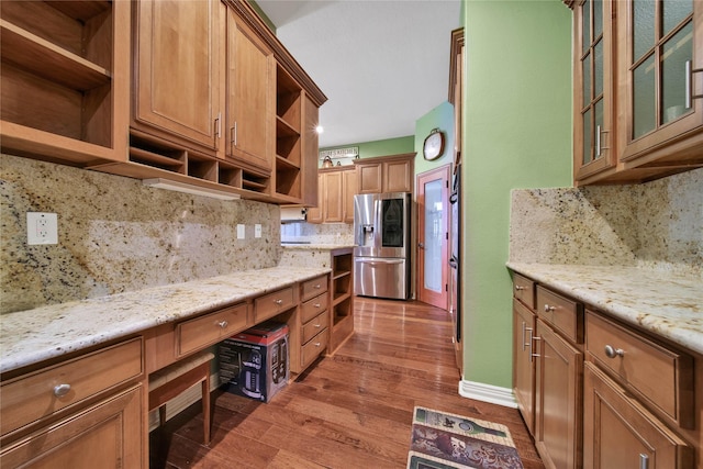 kitchen with decorative backsplash, dark hardwood / wood-style flooring, light stone countertops, and stainless steel refrigerator with ice dispenser