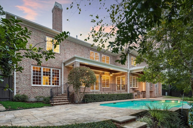 back house at dusk with a fenced in pool and a patio