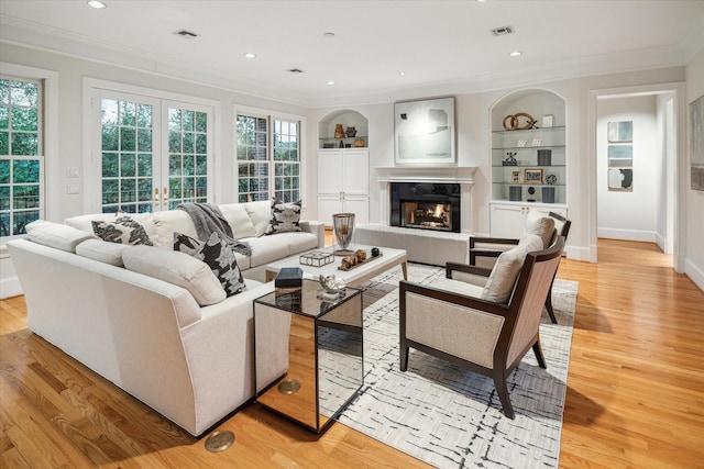 living room with built in shelves, light hardwood / wood-style flooring, and ornamental molding