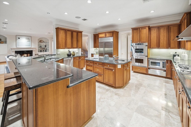 kitchen with a large island with sink, kitchen peninsula, sink, built in appliances, and a breakfast bar area