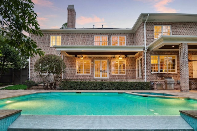 back house at dusk with a fenced in pool, an outdoor kitchen, and a patio