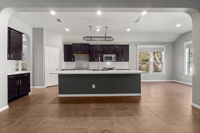 kitchen with a kitchen island with sink, tile patterned floors, vaulted ceiling, dark brown cabinetry, and sink