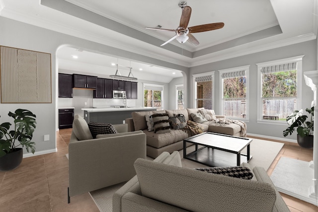 tiled living room featuring ceiling fan, a tray ceiling, ornamental molding, and a healthy amount of sunlight