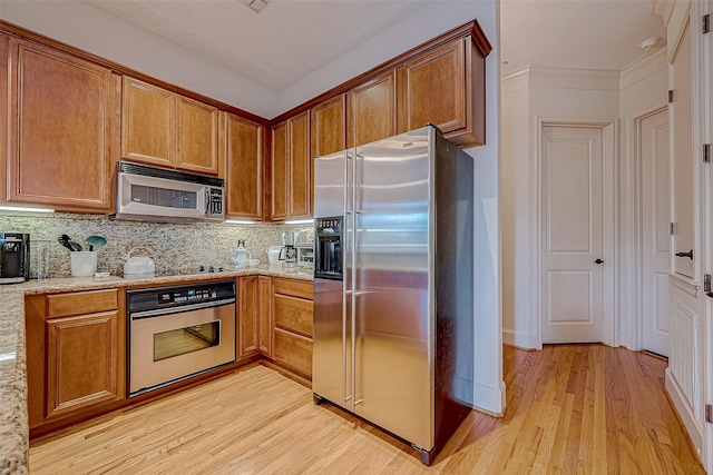 kitchen with tasteful backsplash, light stone counters, light hardwood / wood-style flooring, crown molding, and appliances with stainless steel finishes