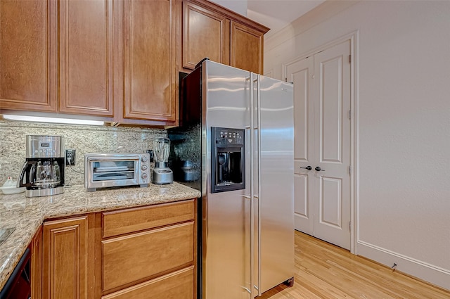 kitchen with tasteful backsplash, light stone counters, stainless steel refrigerator with ice dispenser, light wood-type flooring, and ornamental molding