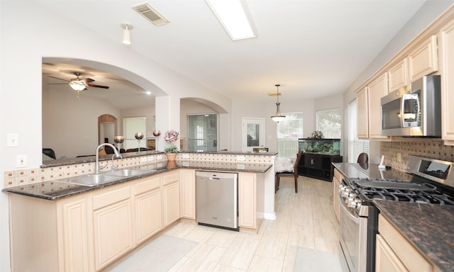 kitchen with appliances with stainless steel finishes, hanging light fixtures, kitchen peninsula, decorative backsplash, and sink