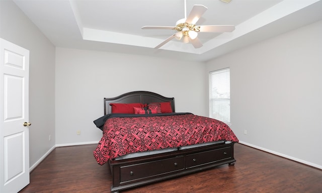 bedroom featuring ceiling fan, dark wood-type flooring, and a tray ceiling