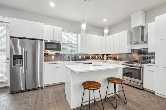 kitchen featuring wall chimney exhaust hood, white cabinets, a center island, and appliances with stainless steel finishes