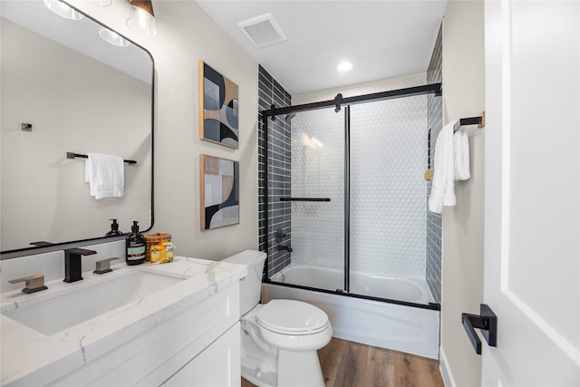 full bathroom with hardwood / wood-style flooring, vanity, enclosed tub / shower combo, and toilet