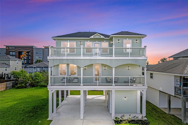 back house at dusk featuring a balcony, a carport, and a lawn