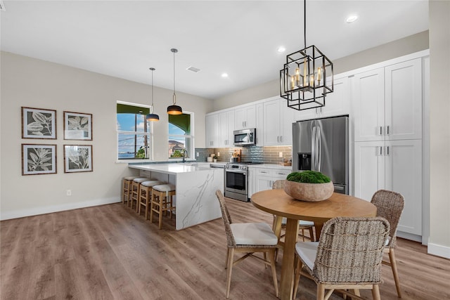 kitchen featuring backsplash, pendant lighting, a breakfast bar area, white cabinets, and appliances with stainless steel finishes