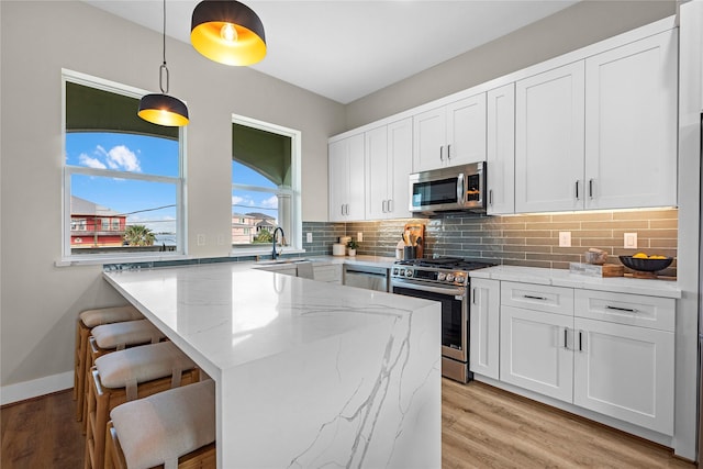 kitchen with a kitchen bar, appliances with stainless steel finishes, light stone counters, white cabinetry, and hanging light fixtures