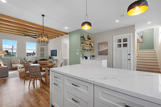 kitchen featuring white cabinets, beam ceiling, light hardwood / wood-style floors, and hanging light fixtures