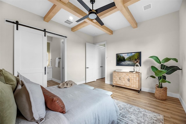 bedroom featuring beamed ceiling, a barn door, ensuite bath, and ceiling fan