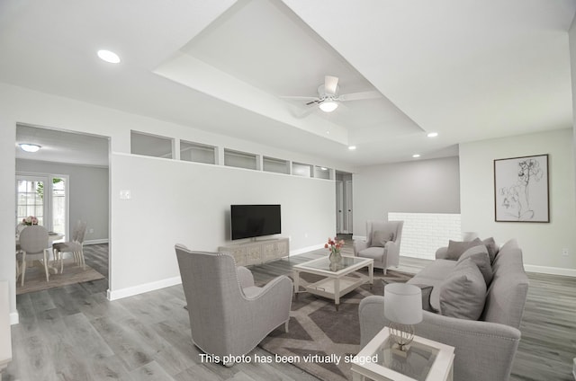 living room with hardwood / wood-style floors, a raised ceiling, and ceiling fan