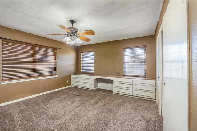 unfurnished office with ceiling fan, light colored carpet, built in desk, and a textured ceiling