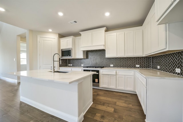 kitchen featuring a sink, stainless steel microwave, dark wood finished floors, white cabinetry, and tasteful backsplash