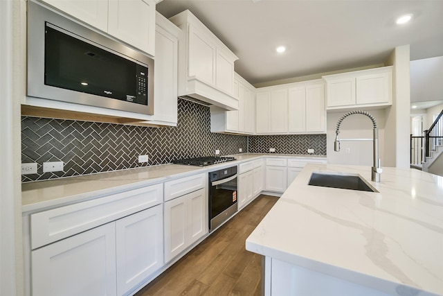 kitchen featuring stainless steel appliances, a sink, white cabinetry, dark wood-style floors, and tasteful backsplash