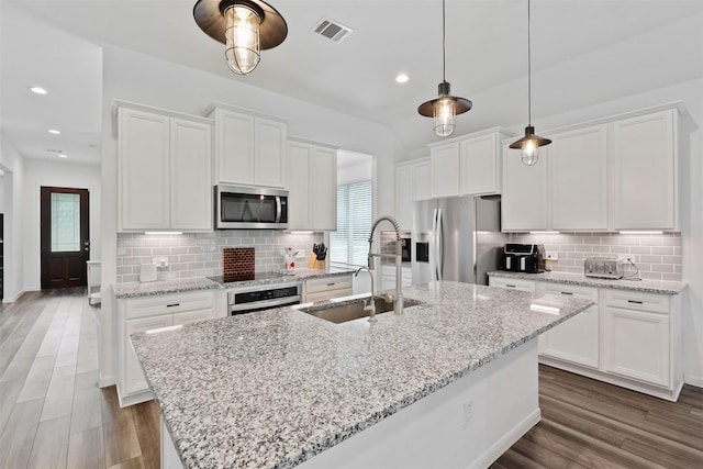 kitchen with stainless steel appliances, a center island with sink, and white cabinetry