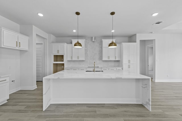 kitchen with sink, light stone counters, a kitchen island with sink, and hanging light fixtures