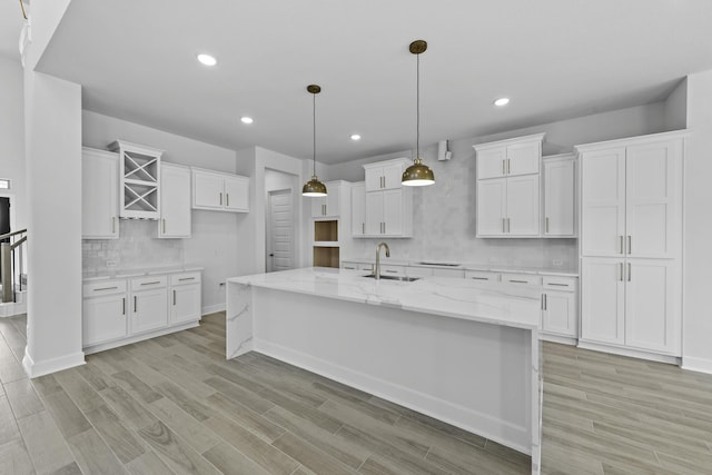 kitchen with light stone countertops, a kitchen island with sink, sink, pendant lighting, and white cabinetry