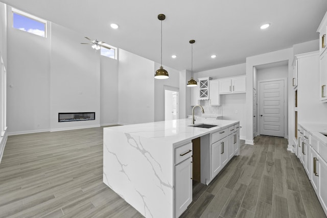 kitchen with ceiling fan, sink, white cabinetry, hanging light fixtures, and an island with sink