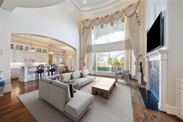 living room featuring a high ceiling, dark wood-type flooring, an inviting chandelier, a fireplace, and crown molding