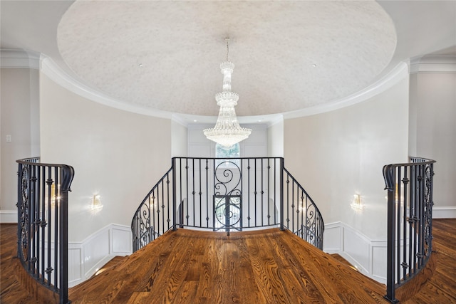 stairs with wood-type flooring, crown molding, and an inviting chandelier