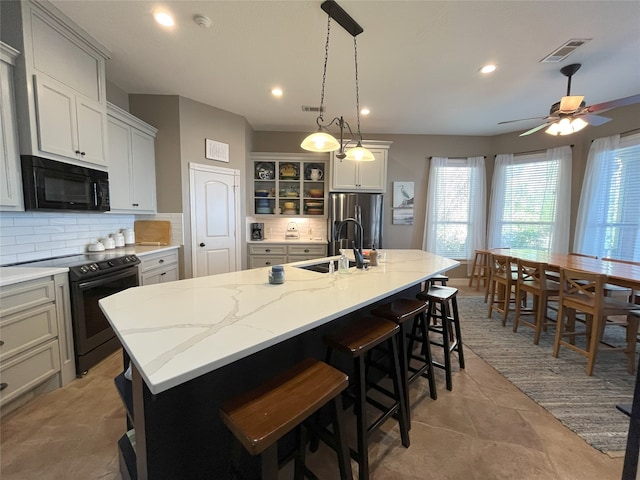 kitchen featuring tasteful backsplash, stainless steel fridge, range with electric cooktop, and an island with sink