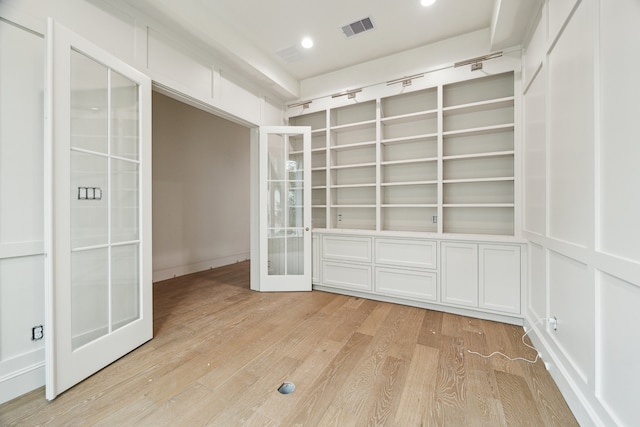 empty room with french doors, built in features, and light hardwood / wood-style flooring