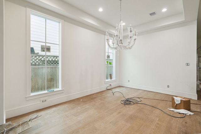 unfurnished dining area with hardwood / wood-style floors, a raised ceiling, and a chandelier