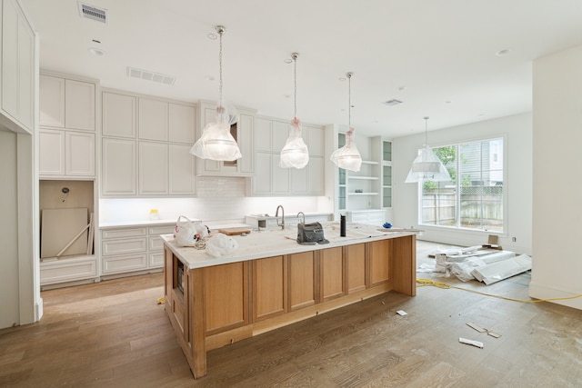 kitchen with a large island, light hardwood / wood-style floors, pendant lighting, light stone counters, and white cabinets