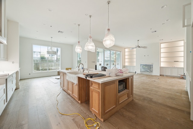 kitchen with white cabinetry, ceiling fan, light hardwood / wood-style flooring, hanging light fixtures, and a center island with sink