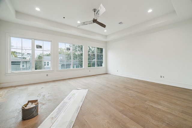 empty room featuring a raised ceiling, ceiling fan, and light hardwood / wood-style flooring