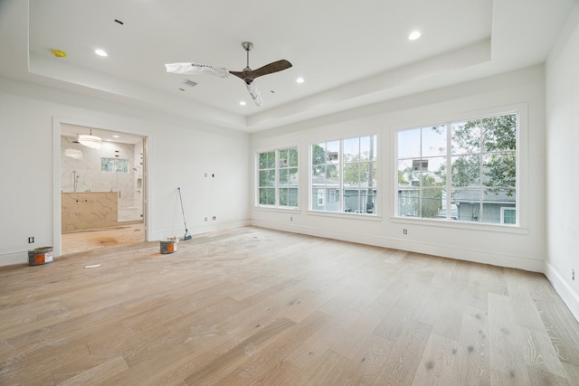 unfurnished living room featuring ceiling fan, light hardwood / wood-style floors, and a tray ceiling