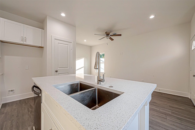 kitchen with light stone counters, dark wood-type flooring, sink, white cabinets, and an island with sink