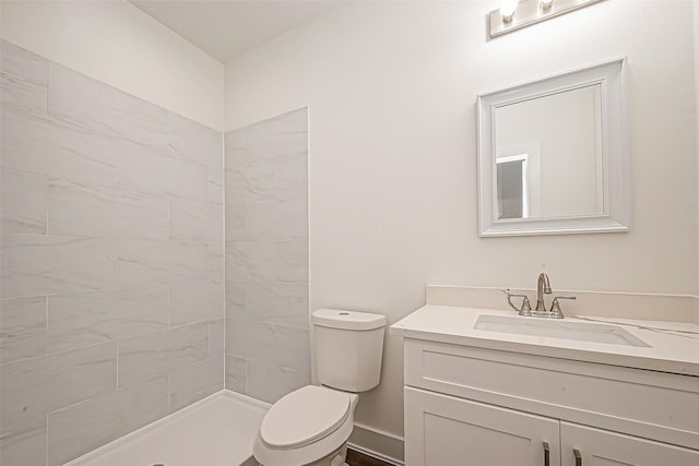 bathroom with a tile shower, vanity, and toilet