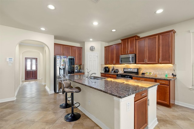 kitchen with appliances with stainless steel finishes, tasteful backsplash, sink, a center island with sink, and dark stone countertops